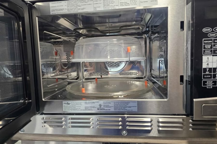 Inside an RV rental's open microwave: stainless steel interior, cooking rack, glass turntable, and part of the control panel. Great for meals.