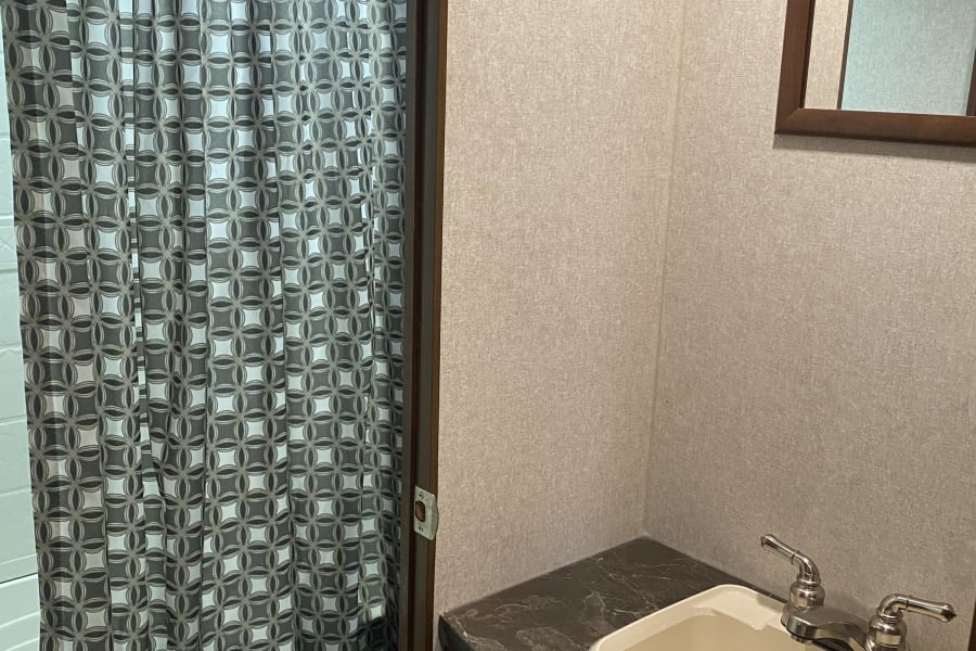 This RV rental bathroom features a geometric shower curtain, compact toilet, sink with faucet, and mirror for your travels.