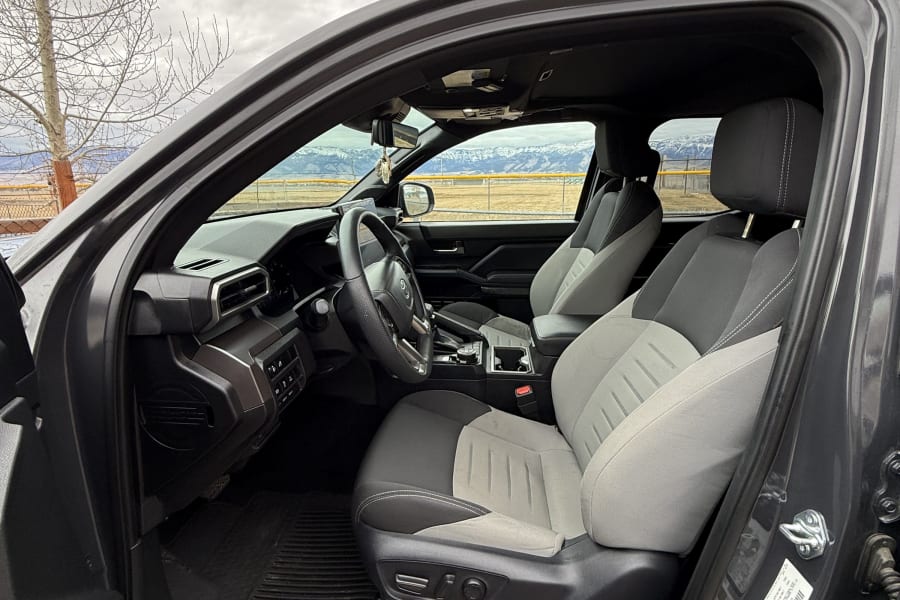 Driver's seat view of a Toyota Tacoma truck's gray/black interior, showing dashboard & steering wheel. Mountains beyond. Perfect for an rv rental trip.