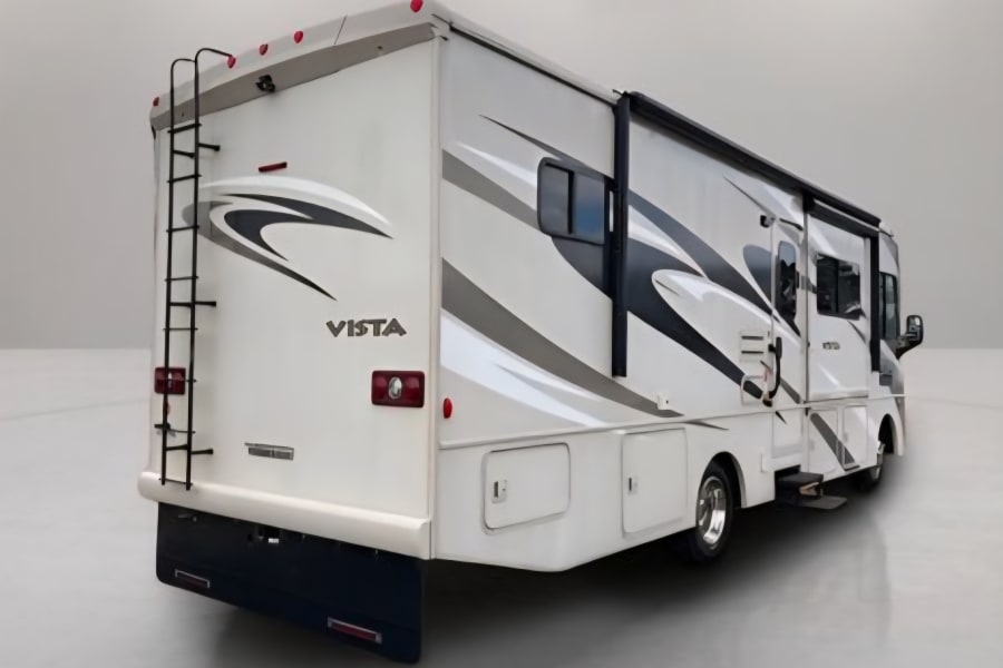 White Vista RV rental, seen from the rear, with graphics, ladder, and extended awning, parked on a gray surface.