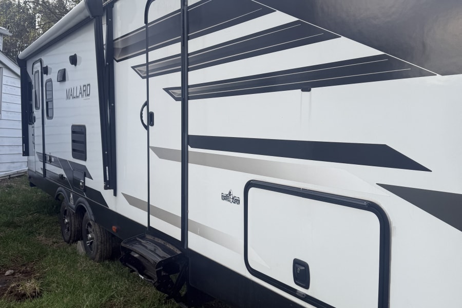 A white and black MALLARD travel trailer RV is parked on a grassy yard. Consider this recreational vehicle for your next rv rental.