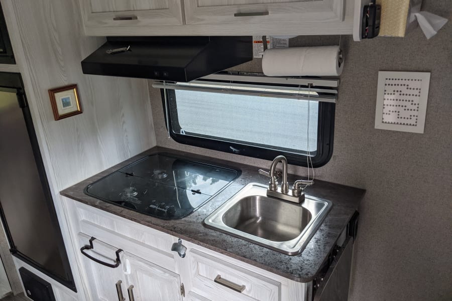 This RV rental galley features a compact kitchen with a sink, stove, overhead cabinets, and a window for natural light.