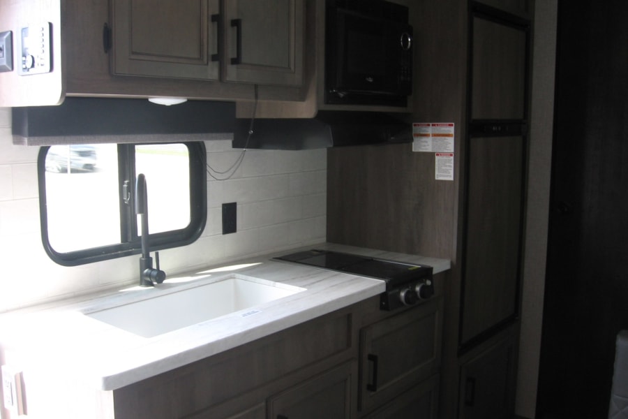 RV rental kitchen: modern design with a white sink, black faucet, two-burner stovetop, microwave, and integrated refrigerator.