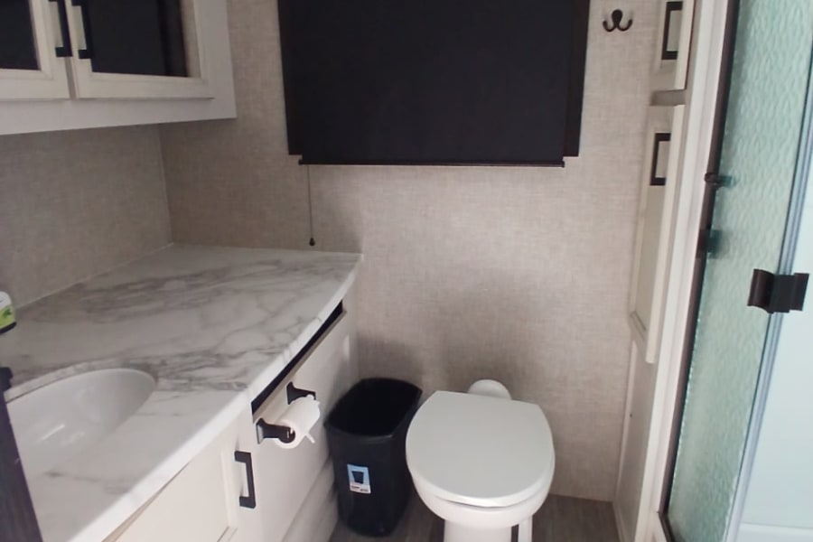 This RV rental bathroom features a sink, toilet, shower stall, mirrored cabinets, and vanity with a light countertop.
