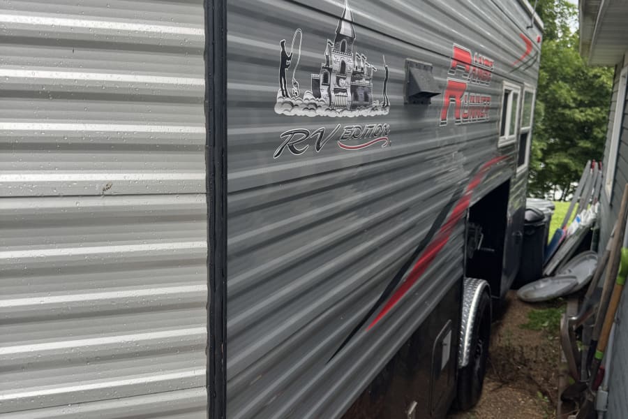 This wet "Ice Castle RV Edition" travel trailer/ice house for rv rental is covered in raindrops, featuring grey siding & red accents.