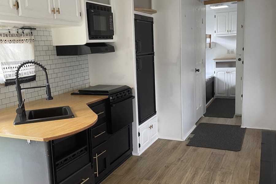 Bright, renovated RV rental interior: a modern kitchen with black & white cabinets, wood counters, & compact appliances.