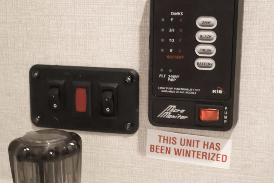 Inside an RV rental: control panel showing water tank levels (gray, black, fresh), battery, and pump switches. Unit is winterized.