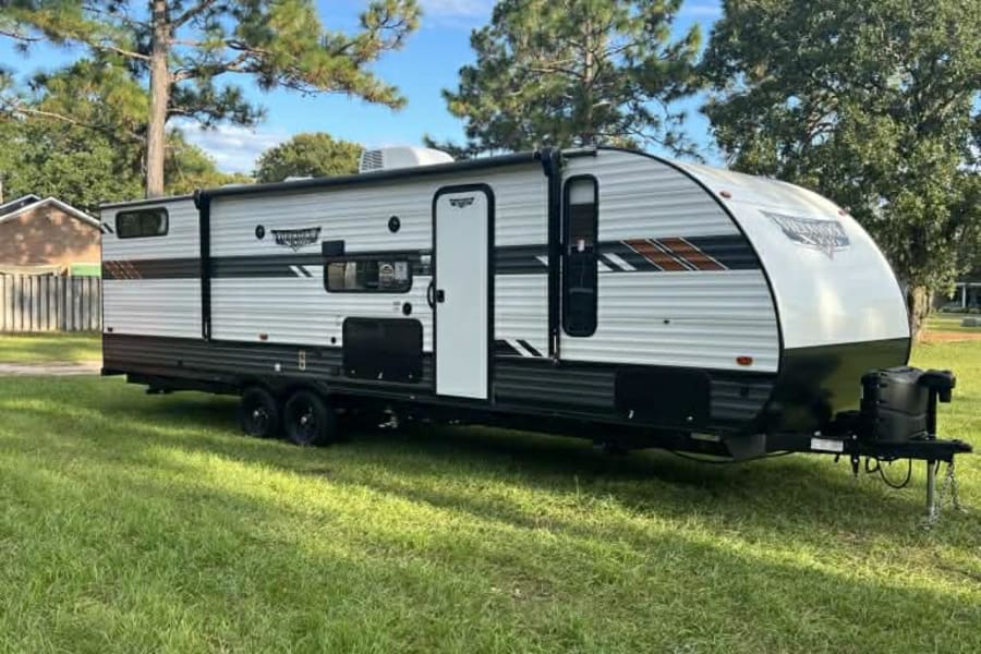 Modern travel trailer, perfect for an RV rental, parked on vibrant green grass under a clear blue sky. Ready for adventure!