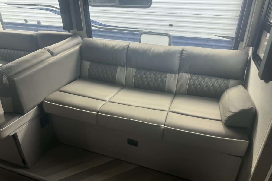 This RV rental features a comfortable gray sofa/dinette with storage, ideal for road trips and relaxing.