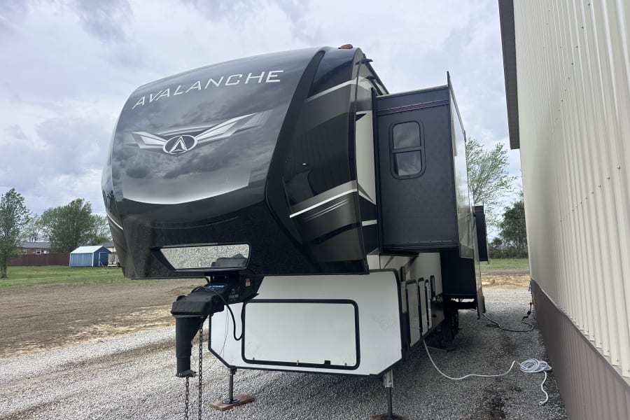 Black Keystone Avalanche fifth-wheel RV rental parked on gravel with extended slide-out and leveling jacks.