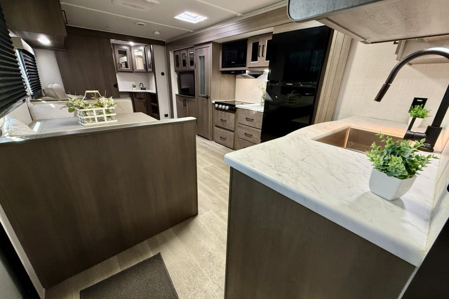 RV rental: Modern interior featuring a kitchen island, sink, stove, microwave, and dining area, ready for adventure.