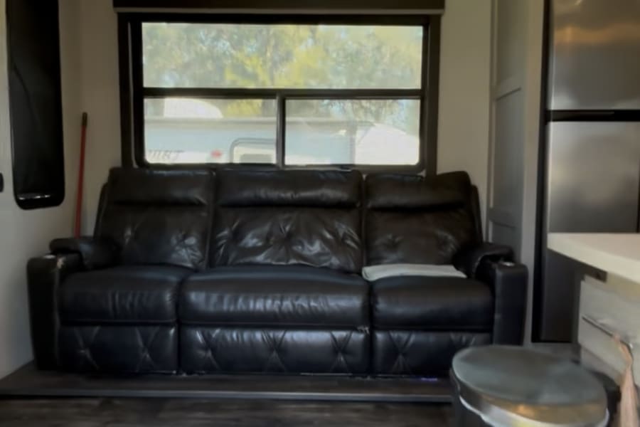 This RV rental boasts a comfortable black leather reclining sofa, large window, and modern kitchen. Perfect for a cozy getaway.