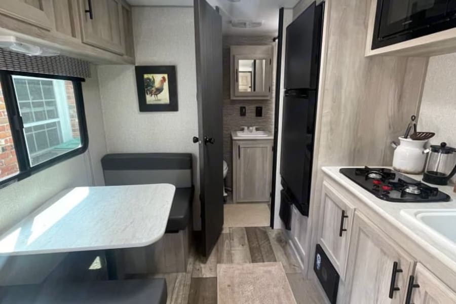 Cozy rv rental interior featuring a bright dinette, full kitchen with stovetop, fridge, and microwave, plus bathroom access.