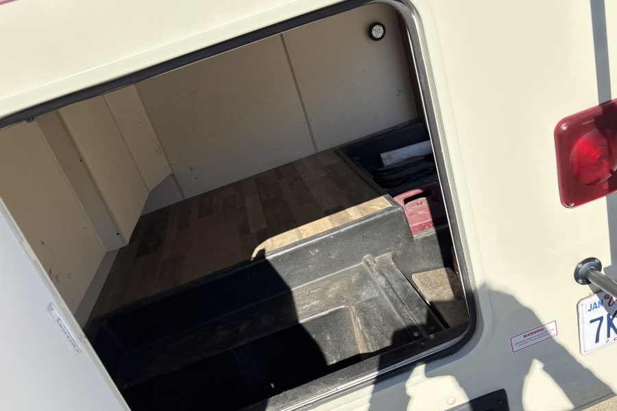 Open RV rental storage compartment with a 250lb load warning. Features a wooden floor and durable plastic tub for gear.