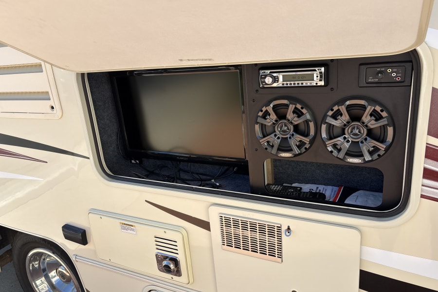 RV rental outdoor entertainment center with TV, Jensen stereo, speakers, and A/V selector in an open compartment.
