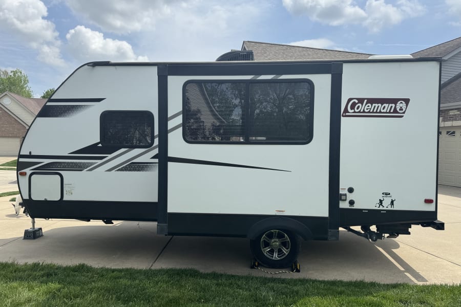 This white Coleman travel trailer, ready for an RV rental adventure, is parked on a driveway with graphic accents.