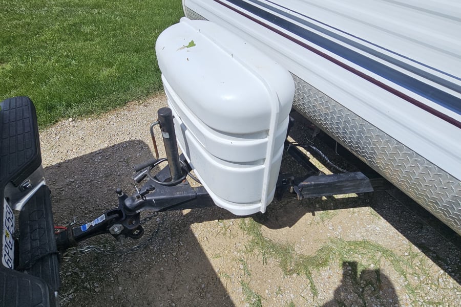 Front view of an RV rental: a white travel trailer hitched to a vehicle, featuring its propane tank cover and diamond plate trim.