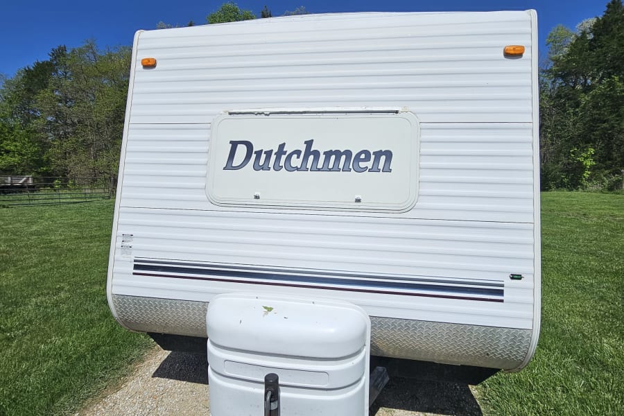 Front view of a white Dutchmen travel trailer, ideal for your next RV rental. Blue sky, green grass & gravel path.