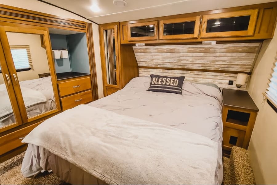 Enjoy this RV rental's comfortable bedroom with a "BLESSED" pillow, plank-style headboard, mirrored wardrobe, and overhead storage.