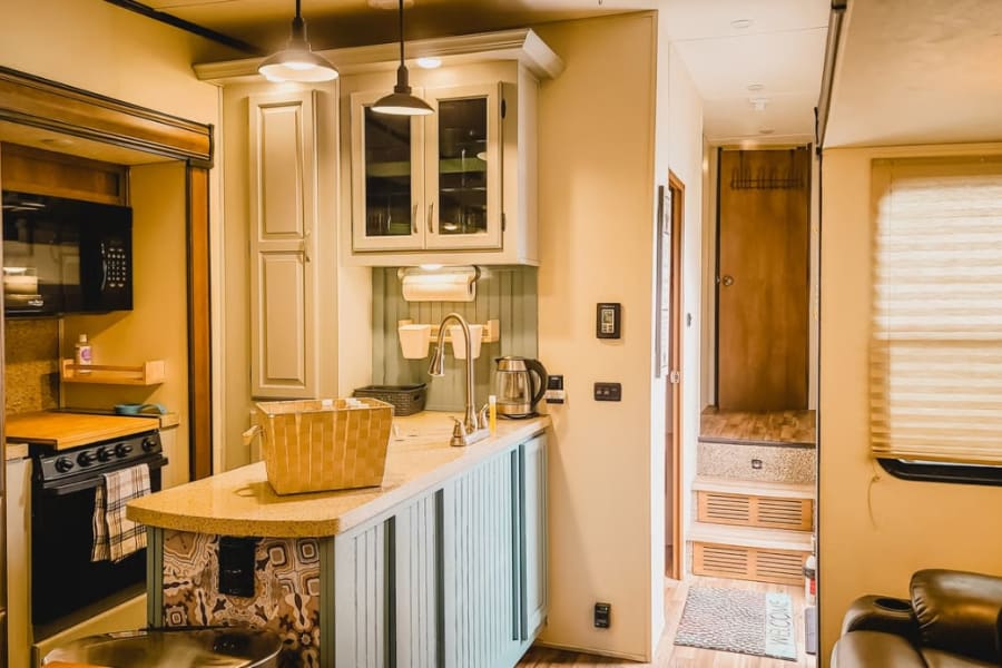 Bright, full kitchen with counter, sink, stove, microwave, and cabinets in an RV rental, plus a hallway with stairs.
