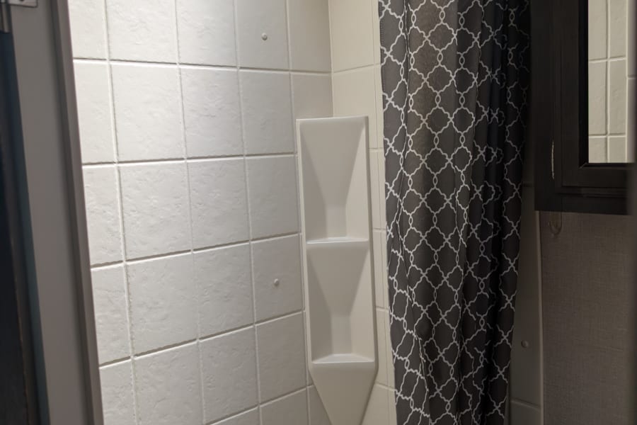 Clean RV rental bathroom featuring a white shower with built-in shelf, bathtub, and patterned curtain.