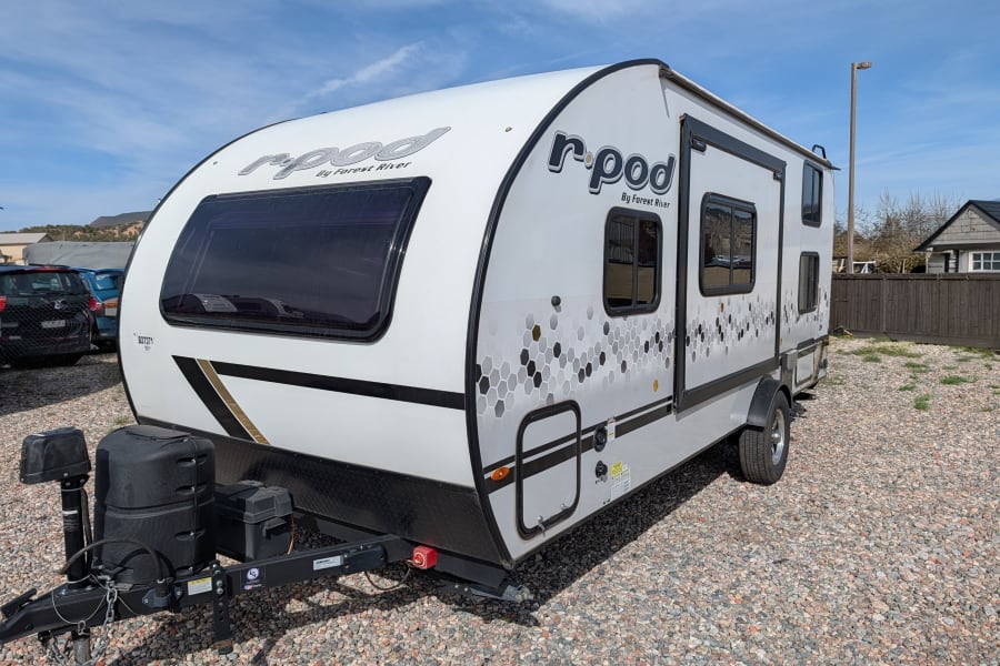 This white r-pod travel trailer, a perfect rv rental, is ready for adventure on a bright day.