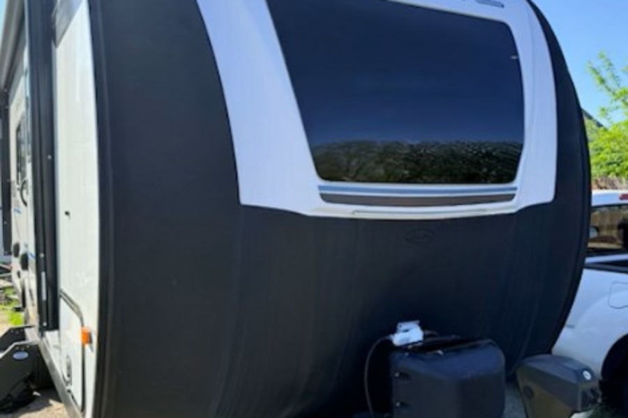 Front of a black and white Real-Lite travel trailer RV rental, featuring a large window, propane tanks, and a hitch for outdoor adventures.