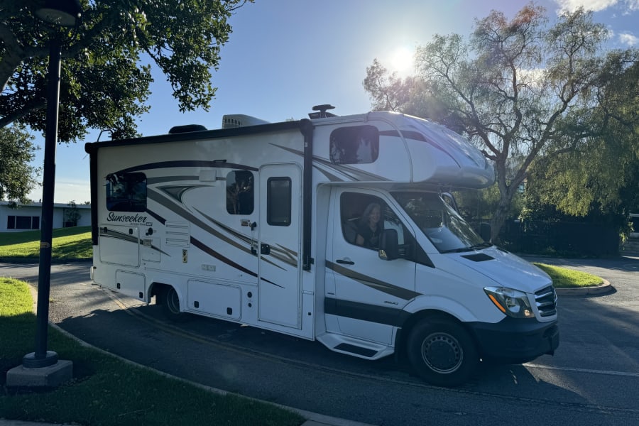 A smiling woman drives a white Forest River Sunseeker RV, an ideal rv rental for your next road trip adventure.