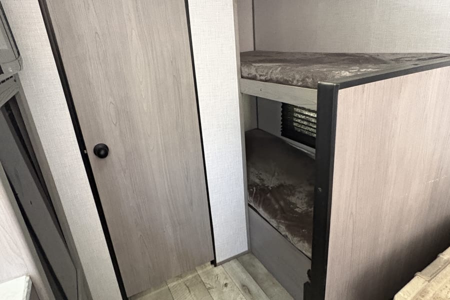 This RV rental interior showcases a light wood-look door, bunk beds, and matching flooring, creating a compact living space.