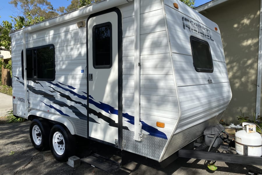 This white Carson Rebel rv rental travel trailer, with blue graphics & dual axles, is ready for your next adventure.