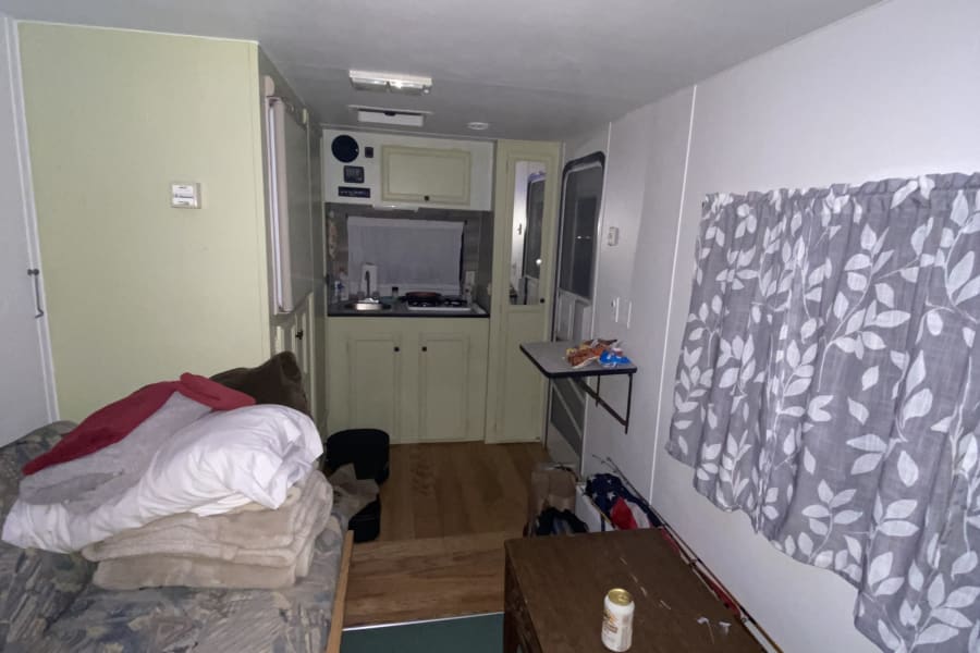 Inside a compact RV rental featuring a bed, small kitchen, dining table, and fishing equipment.