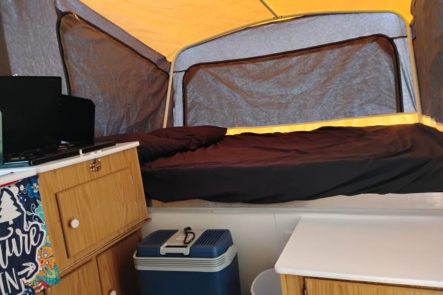 Cozy rv rental pop-up camper interior: features a comfortable bed, mini kitchen area, and cooler for your adventure.
