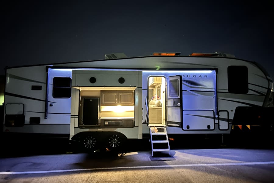 This cozy Cougar rv rental lights up the night, revealing an outdoor kitchen, welcoming interior, and starlit sky.
