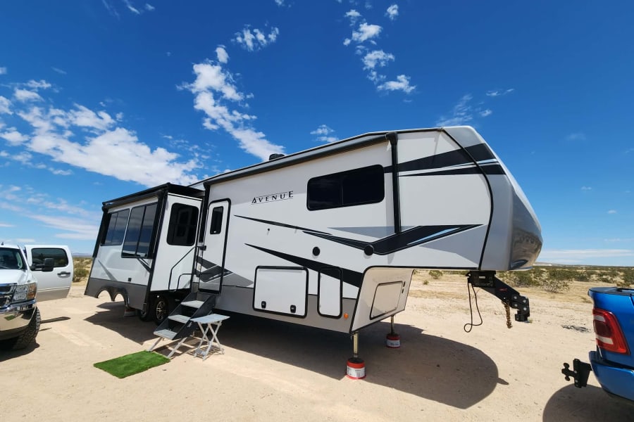 Modern white fifth-wheel RV rental parked in a sunny desert, ready for adventure under a blue sky.