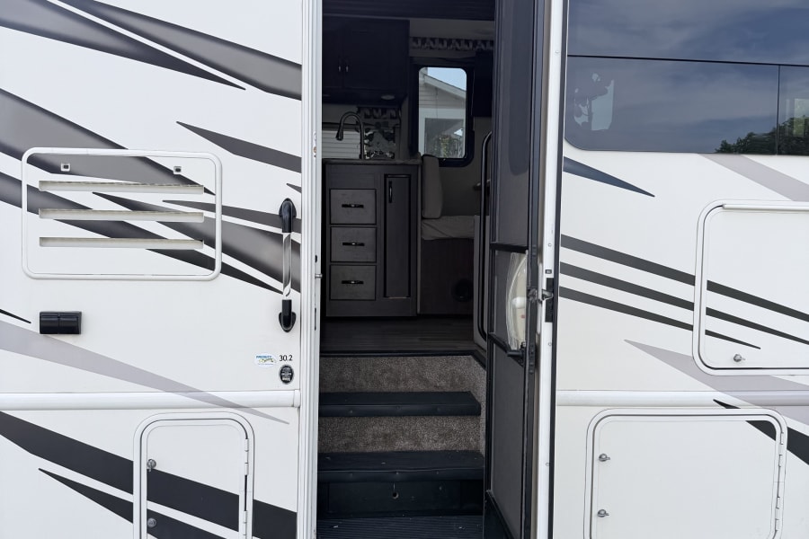 An open door reveals the inviting interior of an RV rental, with entry steps, a kitchen, and a dinette for your travels.
