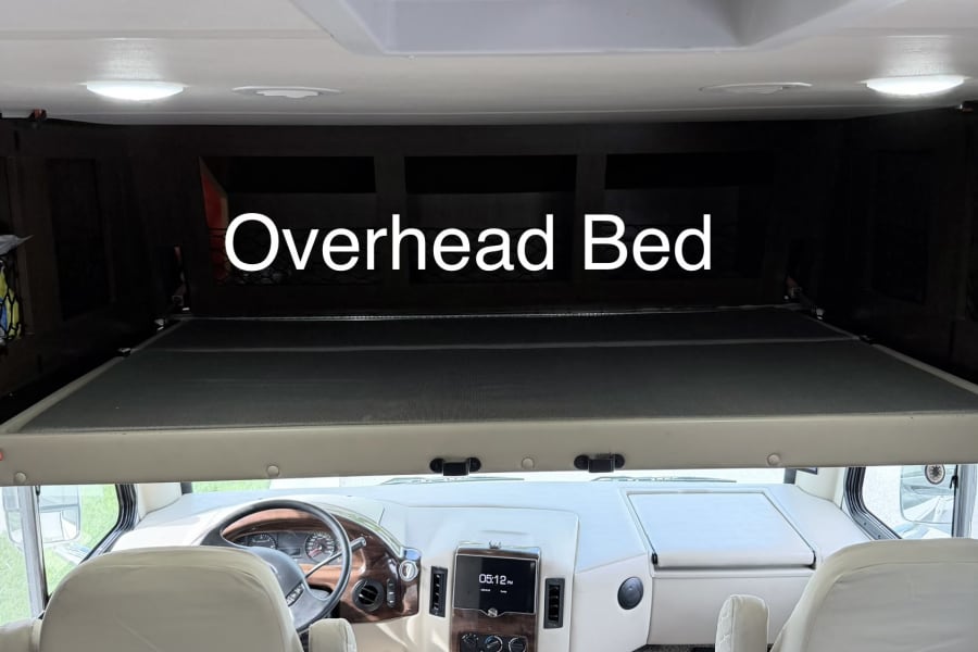 RV rental interior: driver's cockpit with captain chairs and a lowered overhead bed, providing extra sleeping space in this motorhome.