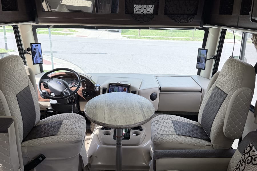 Inside a modern RV rental: the driver's cockpit, a central table, and plush seating in the living area are visible.