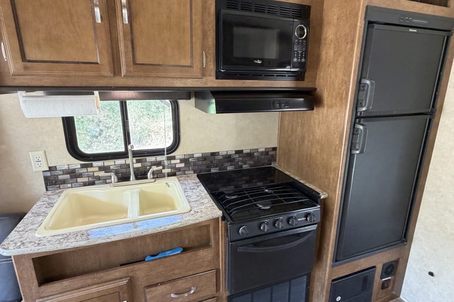 An rv rental kitchen with wood cabinets, double sink, microwave, stove, and refrigerator. Features floor tie-downs.