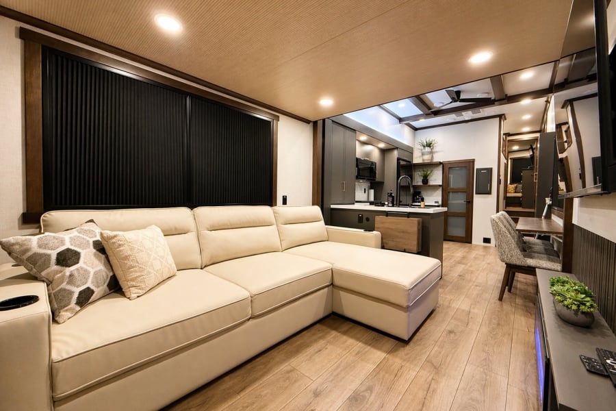 Spacious, modern RV rental interior featuring a comfortable cream sectional, full kitchen, and dining area with wood floors.