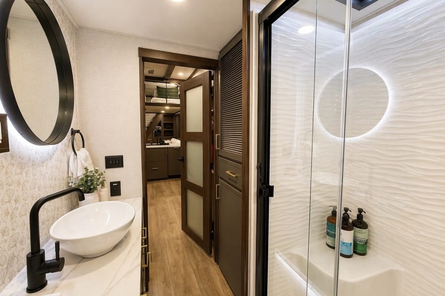 Inside a luxurious RV rental bathroom: chic vanity with vessel sink, backlit mirror, and a wavy-textured shower wall.