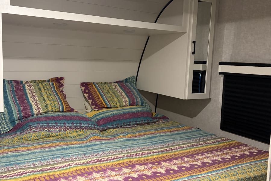 Cozy RV rental bedroom with colorful patterned bedding, overhead storage, and AC unit for a comfortable stay.