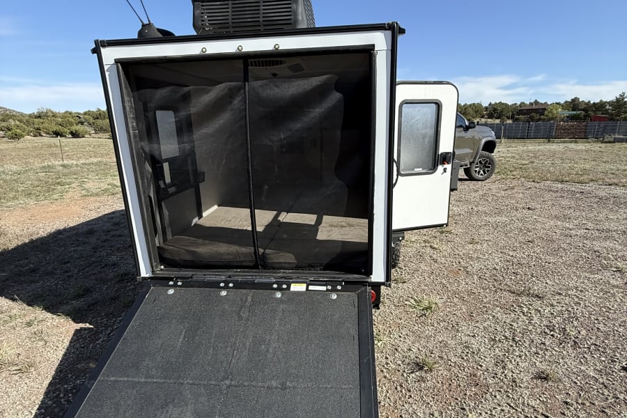 An rv rental with a lowered ramp and screen door. This compact trailer features a roof AC unit and antenna, ready for camping.