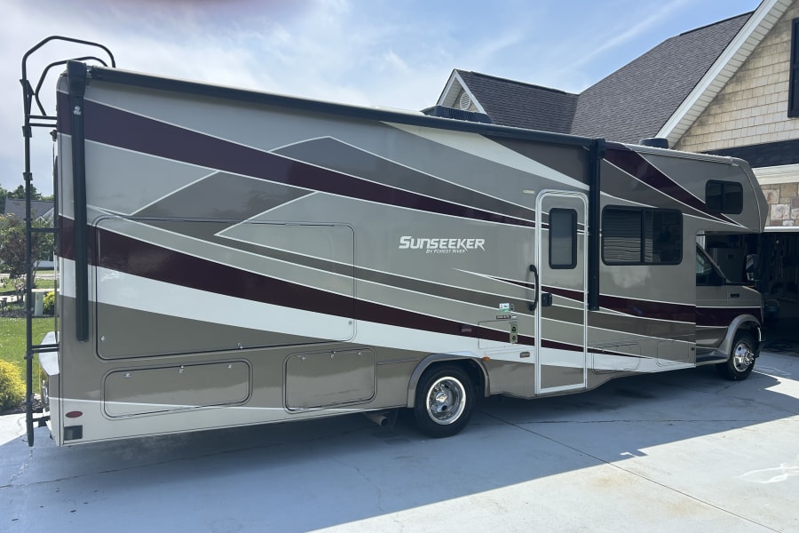 A tan, maroon, and gray Sunseeker RV rental with geometric stripes is parked on a driveway, ready for travel.