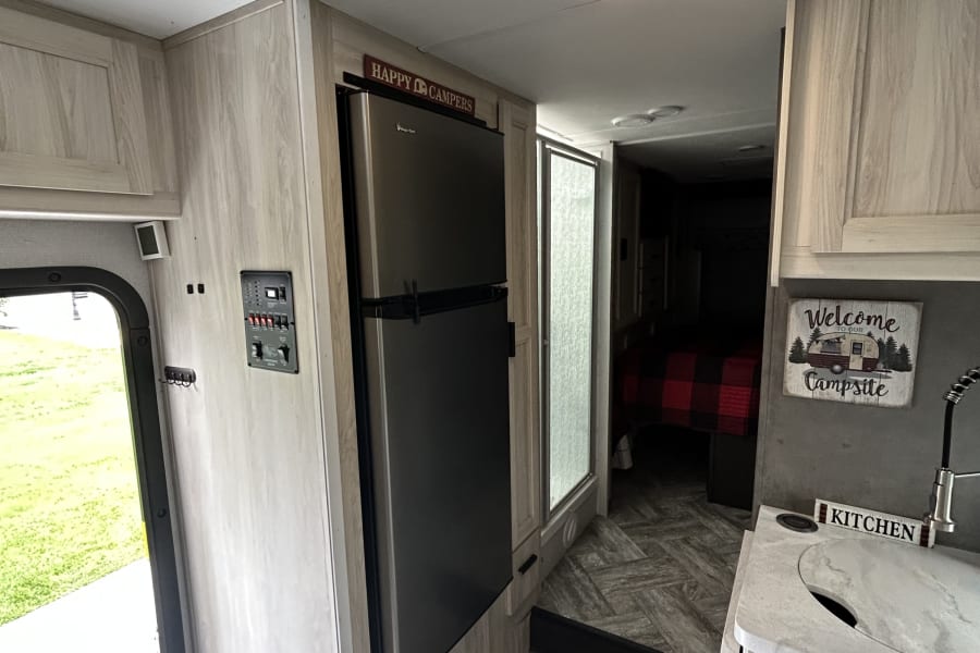 Explore this bright rv rental interior with a kitchen, fridge, control panel, and a cozy bedroom in the back.