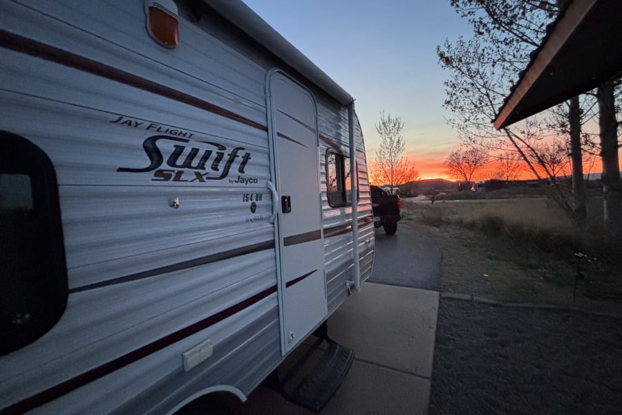 Stunning sunset over an RV rental: a Jayco travel trailer parked in nature with a vivid orange and red sky.