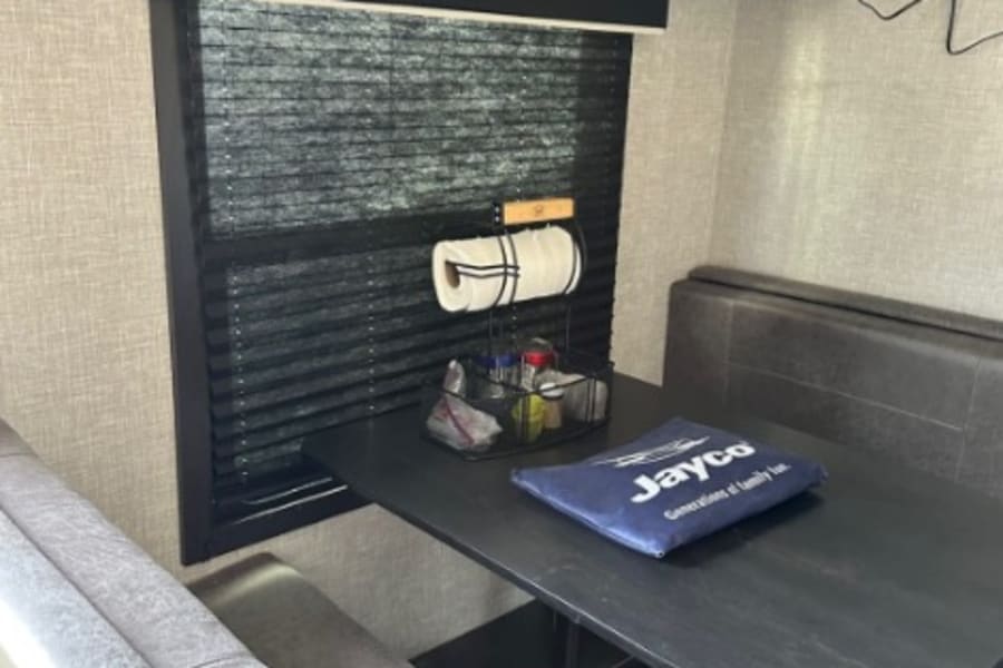 Cozy RV rental interior: a dinette with a dark table, bench seats, window, and overhead cabinets, ideal for travel adventures.