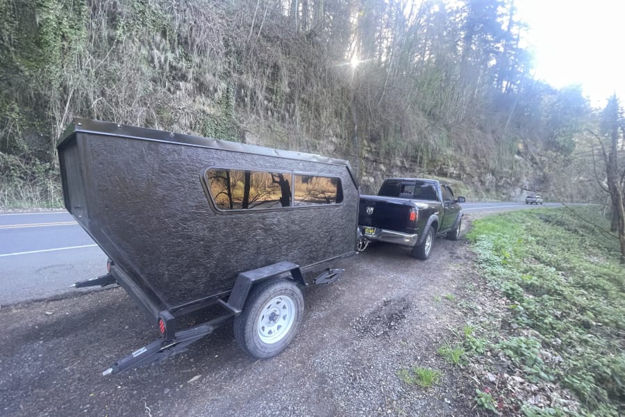 Black truck pulling a textured camper trailer on a scenic road. This compact RV rental is ready for outdoor adventures.