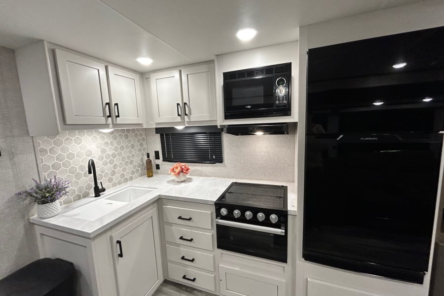 Modern RV rental kitchen features light cabinets, black appliances, and hexagon tile backsplash. Bright and functional.