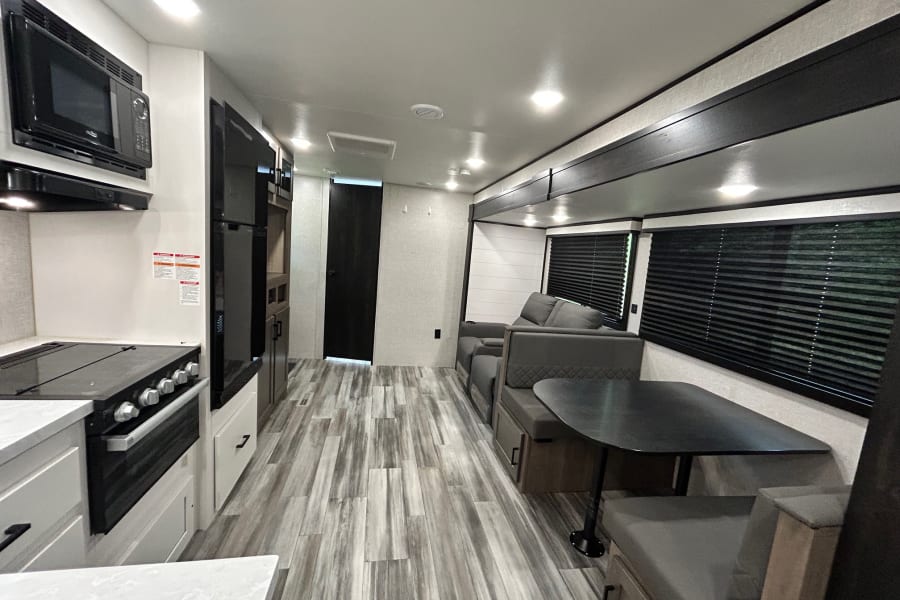 Bright RV rental interior showing a modern kitchen, dinette with dark table, and grey sofa in a spacious living area.