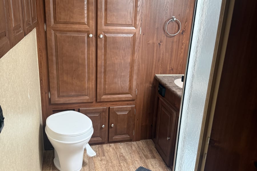 RV rental bathroom: compact toilet, wooden storage, sink, and shower stall, offering functional comfort.